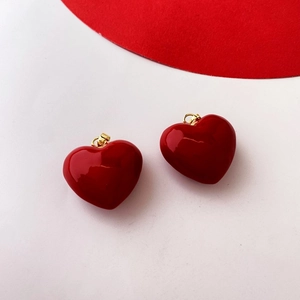 Close-up of two polished red heart pendants with gold clasps on white background