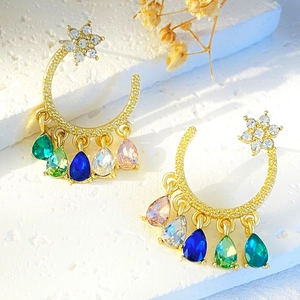 Detail of star-moon earrings with five colorful teardrop stones on a white stone background
