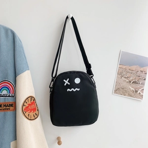 Détail d'un sac bandoulière en toile noire avec imprimé graphique blanc sur mur blanc