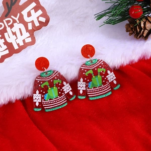 Macro view of Christmas red sweater acrylic earrings with glitter and festive pine background