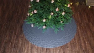 Close-up of dark grey knitted Christmas tree skirt with cable knit pattern on wood floor