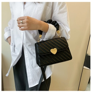 Model wearing a black quilted handbag with heart-shaped lock and adjustable strap