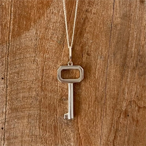 Macro view of sterling silver key pendant hanging over rustic brown wood texture