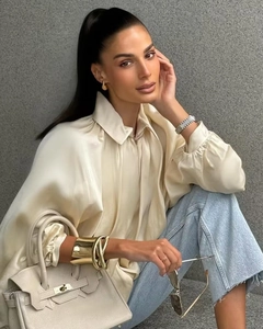 Detail of cream silk blouse paired with light blue jeans and leather handbag