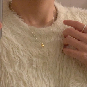 Close-up of minimalist gold heart pendant on silver chain worn over a white knit sweater