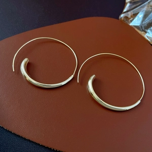 Detailed macro of gold hoop earrings with curved profile on leather texture background