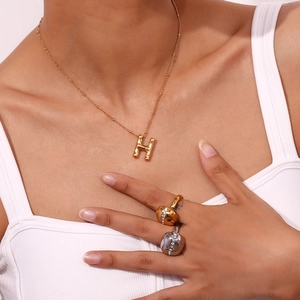 Detail of gold H letter pendant necklace and shimmering rhinestone open rings set