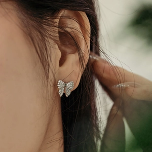 Macro shot of silver bow stud earrings with sparkling zircons worn on earlobe