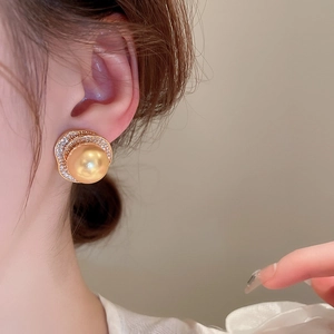 Gros plan d'une boucle d'oreille en perle dorée avec bord ondulé en zircons sur un modèle
