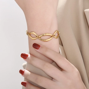 Close-up of a chunky gold chain bracelet worn with a beige blazer for a chic look