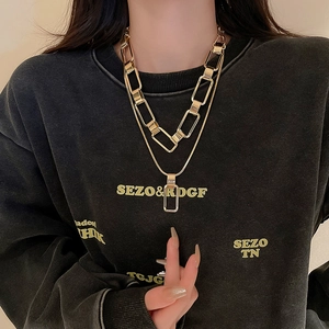 Detail of layered gold metal chain necklace with chunky link and square pendant