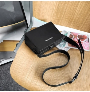 Close-up of black leather box bag with silver hardware on a desk with magazines