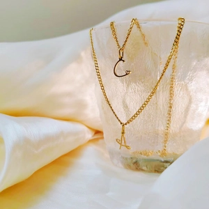Close-up of gold stainless steel Cuban chain necklace featuring heart initial pendants A and C
