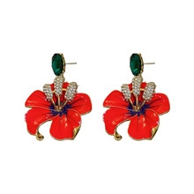 Elegant flower earrings with orange petals and green gems on a clean white background