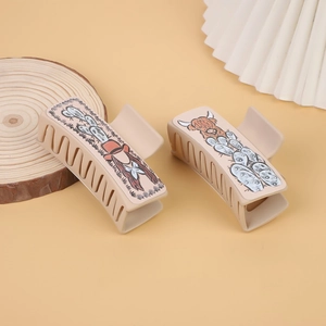 Detail of beige western cowboy style hair claws featuring cartoon desert cow and cactus motifs