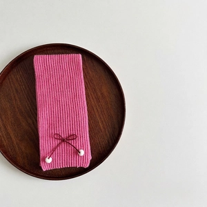 Detail of pink knit scarf with bow and white pompoms on a wooden tray