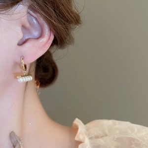 Close-up of elegant gold plated geometric earrings with four round white pearls on a model