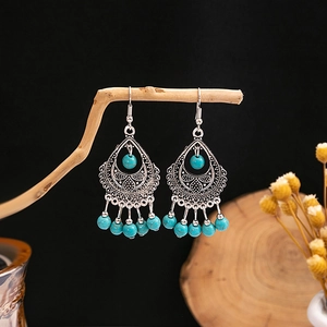 Close-up of Bohemian earrings with blue beads and silver tassels on a rustic branch