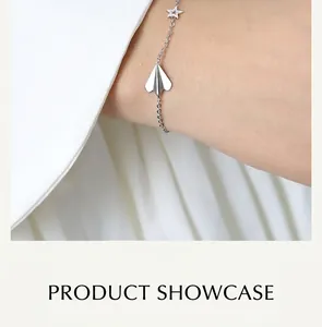 Close-up of a silver bracelet featuring paper plane and star charms on a woman's wrist