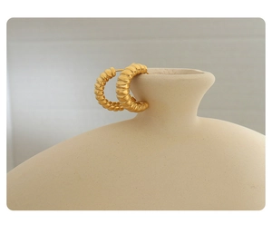 Macro detail of gold-plated croissant hoop earrings with a textured ribbed C-shape design