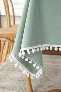 Close-up of sage green washed cotton tablecloth with white pom-pom fringe details