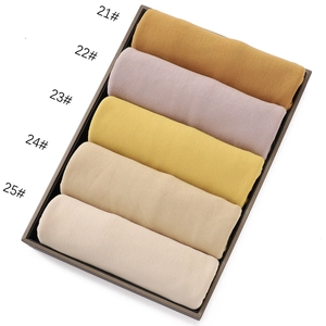 Detail view of five rolled jersey cotton scarves in soft pastel colors in a display box