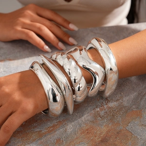 Close-up of five chunky silver irregular geometric bangles with mirror finish texture