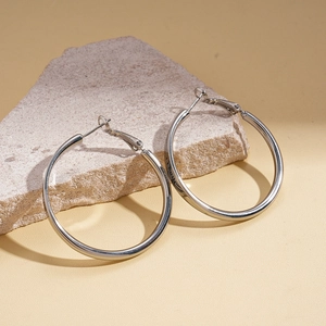 Detailed view of silver hoop earrings with engraved lettering on textured stone surface