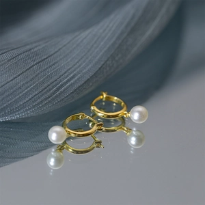 Detailed shot of elegant gold pearl drop earrings on blue silk with mirror reflection