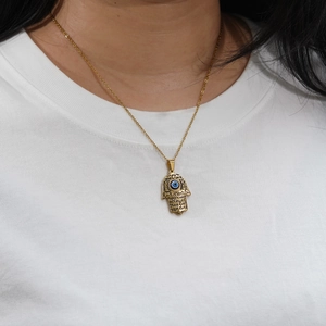 Gold Hamsa Hand necklace with blue Evil Eye pendant worn on a white T-shirt