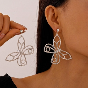 Macro view of silver butterfly earrings with sparkly zircons shown on hand and ear