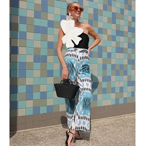 Detail of one-shoulder black swimsuit with large 3D white flower and printed trousers