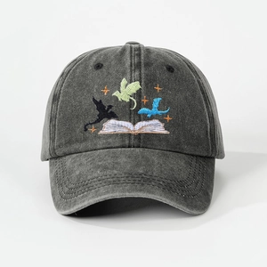 Macro detail showing embroidered flying dragons and open book on washed grey baseball cap