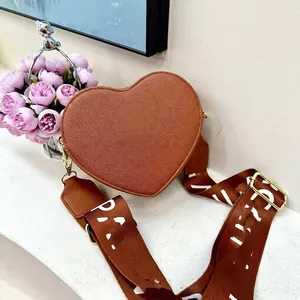 Brown heart-shaped crossbody bag with a wide patterned strap and leather texture