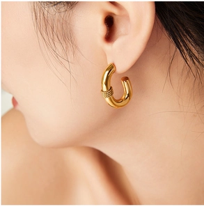 Close-up of gold-plated thick U-shaped hoop earrings with braided texture detail