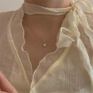 Close-up of a heart-shaped crystal pendant on a gold necklace worn by a model