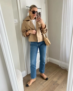 Chic women's spring outfit with short khaki double-breasted trench coat and blue denim jeans