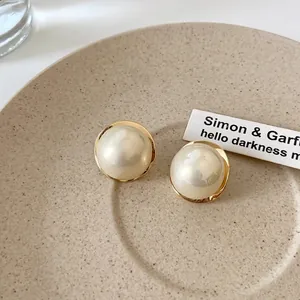 Boucles d'oreilles dorées avec grandes perles blanches sur un plateau en céramique