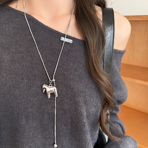Detail of silver pony pendant on Y-shaped necklace worn over a grey knit sweater