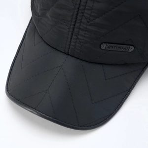 Macro view of quilted black baseball cap with metallic logo plate and stitch details