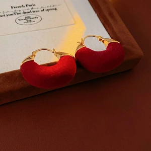 Macro shot of U-shaped earrings featuring red velvet texture and gold-plated metallic accents
