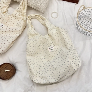 Détail de sacs cabas en velours côtelé à fleurs bleues et rouges sur lit blanc