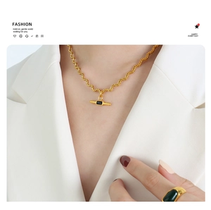 Detail of gold rope chain necklace with black rectangular pendant and emerald stone ring