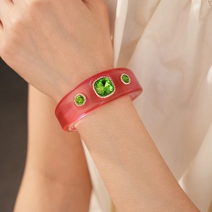 Close-up of pink resin bangle with green crystals and sparkling pavé accents
