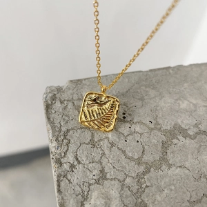 Macro shot of gold square pendant with leaf texture resting on a textured gray stone