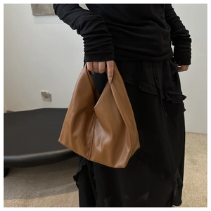 Chic triangle pleated bucket bag in caramel brown leather held by a model in black