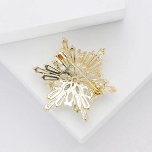 Detailed view of gold snowflake brooch with sparkling zircons on white platform