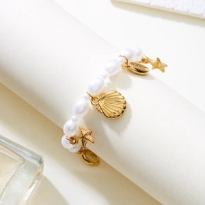 Detail of bohemian pearl bracelet with golden starfish and seashell charms on white stand