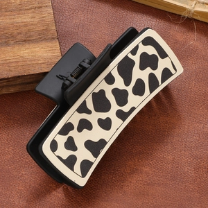 Minimalist matte black hair claw clip with contrast cow print pattern on leather backdrop