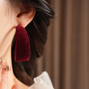 Close-up of deep red velvet C-shaped earring worn by a model in soft lighting